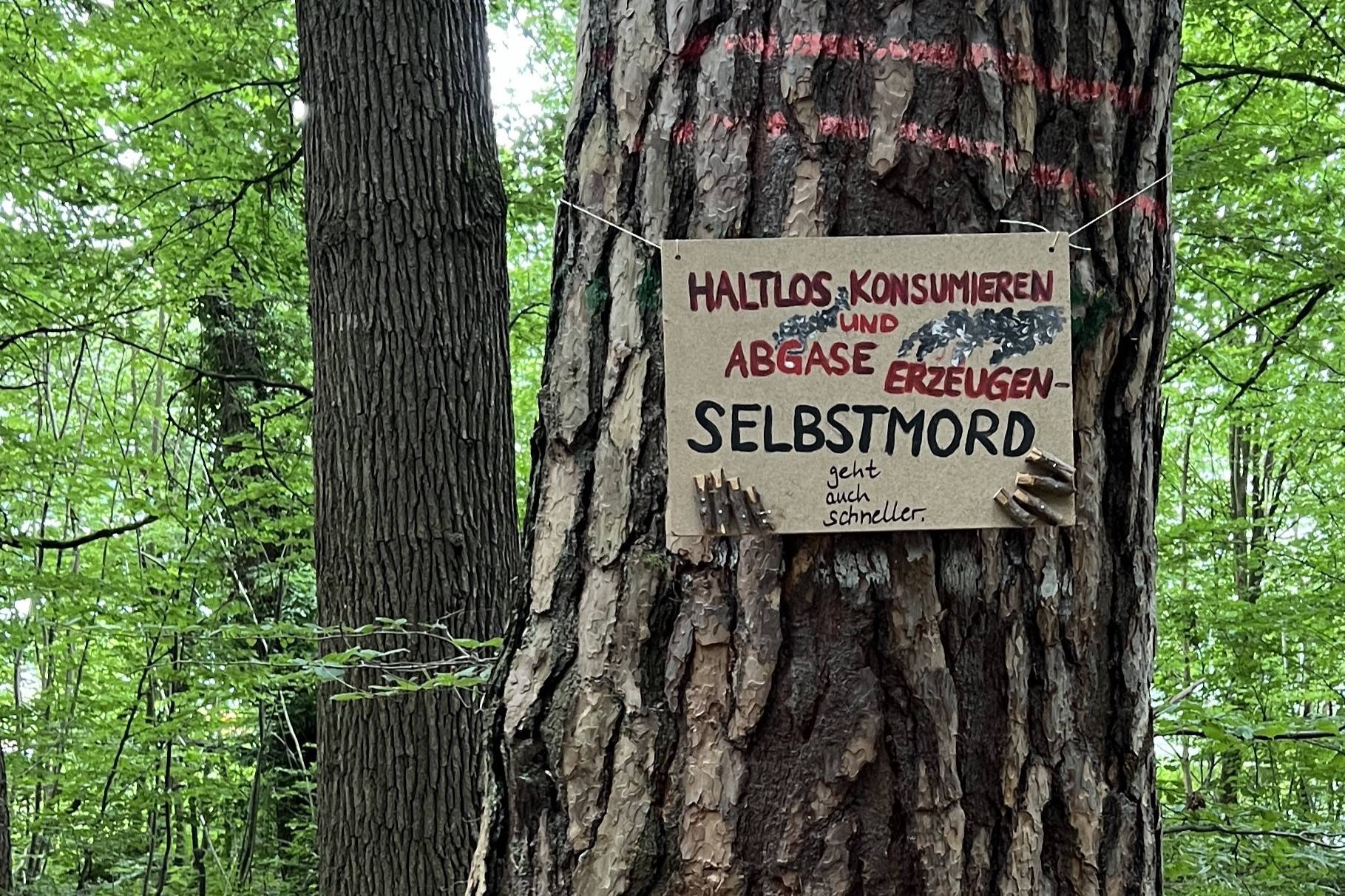 Baumschild 'Haltlos konsumieren und Abgase erzeugen - Selbstmord geht auch schneller'